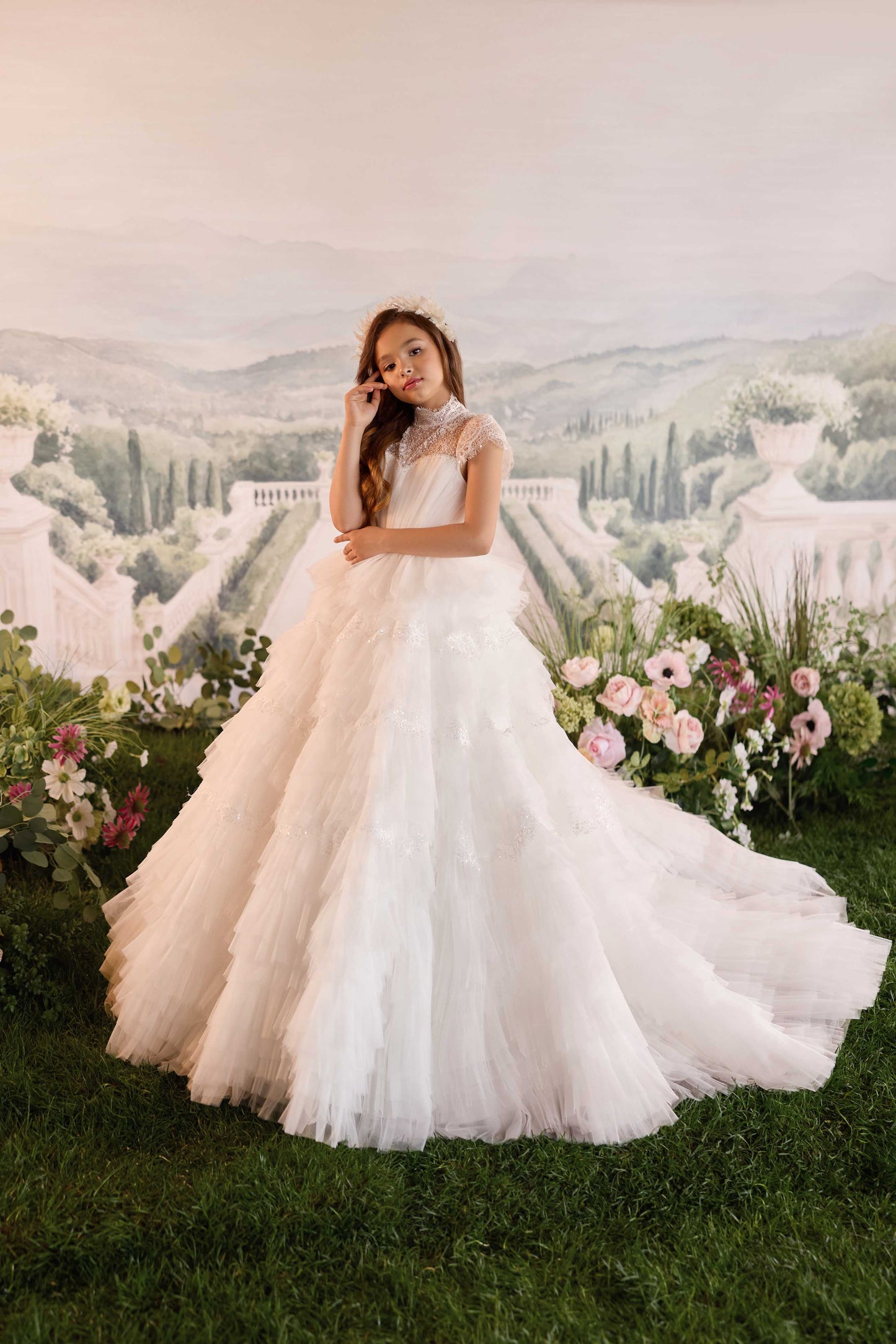 Little girl modeling a luxury ivory white high-neck ball gown with a tiered tulle skirt and beaded lace bodice.