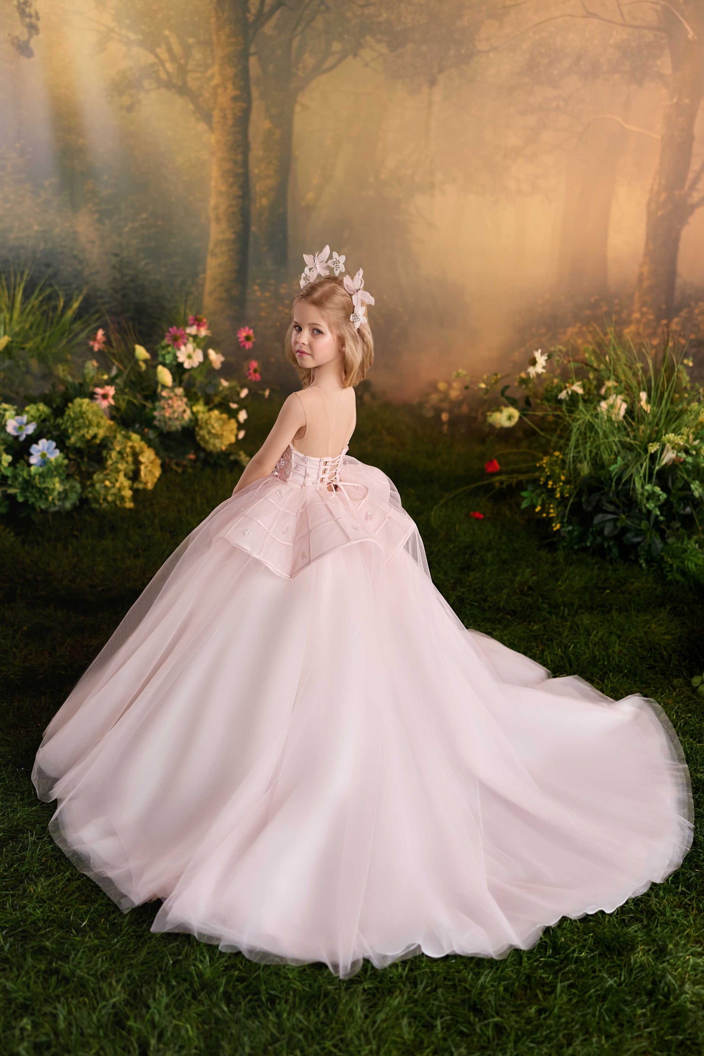 Back view of a premium tulle flower girl gown showcasing the long, voluminous sweeping train trailing on the grass.