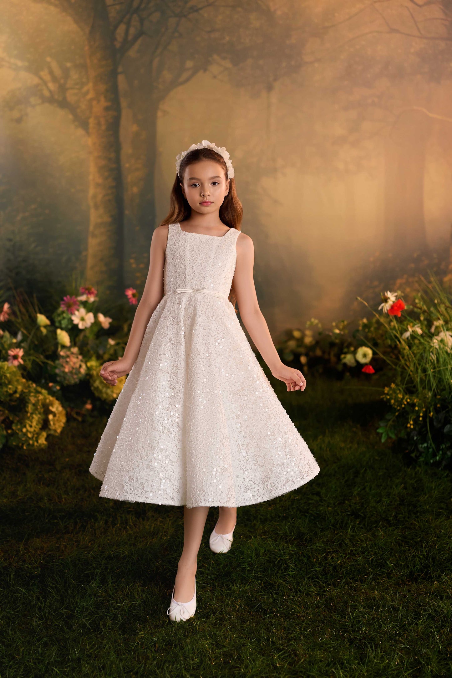 Detailed close-up of the shimmering textured overlay fabric and intricate stitching on a girl's white formal dress.