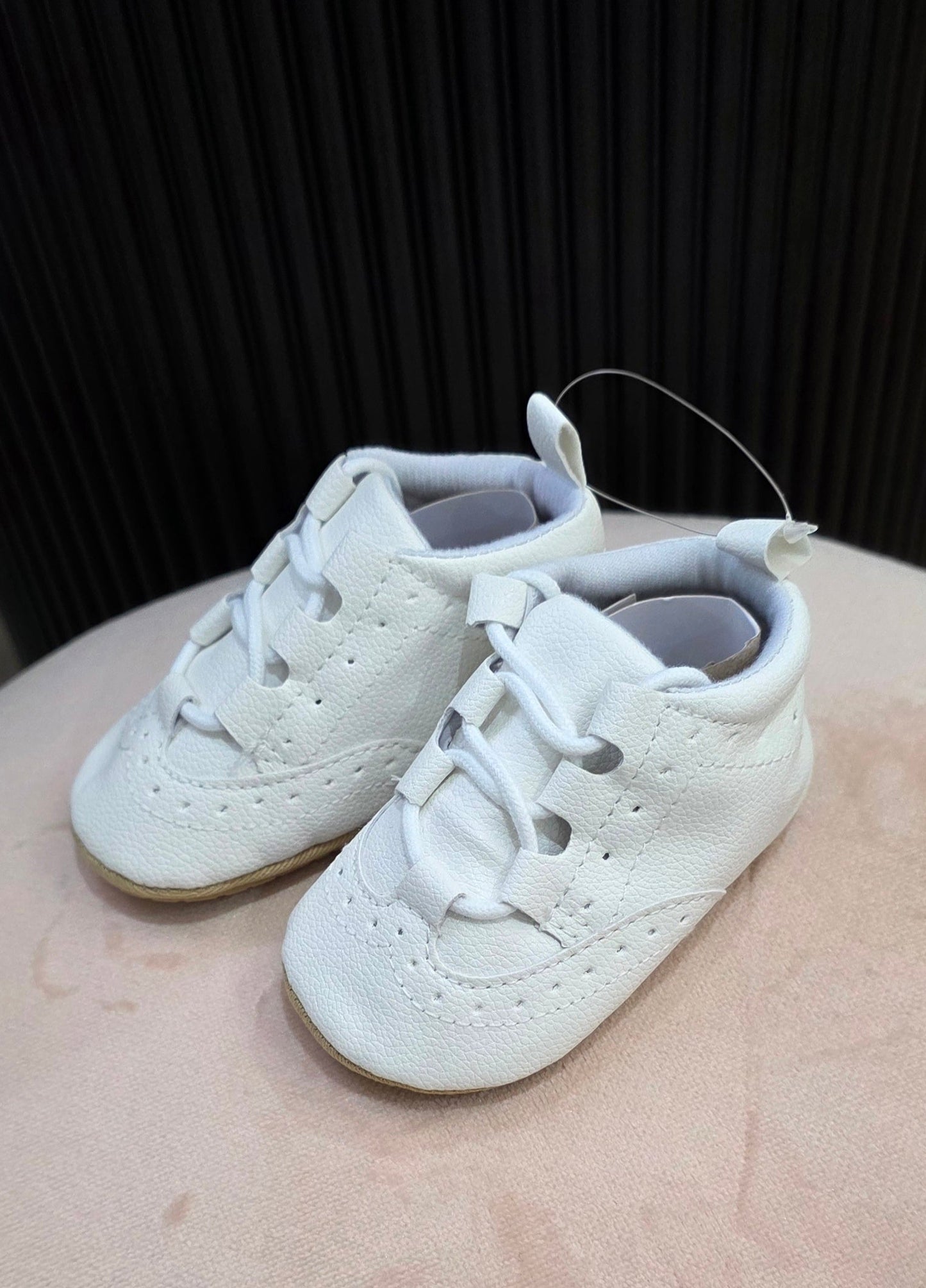 White baby shoes on a beige surface with a dark background