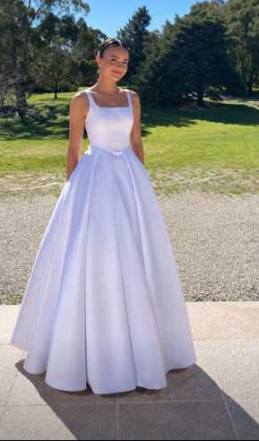 Young woman wearing an elegant white debutante ball gown with a square neckline, fitted bodice, delicate straps and full pleated floor-length skirt.